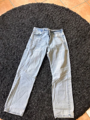 Ljusblå raka jeans - Säljer ett par ljusblå jeans med rak passform och klassisk femficksdesign. Jeansen har normal midja och är tillverkade i denim. Perfekta för en avslappnad och trendig look.