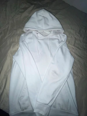 Vit hoodie från Pier One - Klassisk vit hoodie från Pier One med huva och dragsnören. Hoodien har en stor magficka och ribbade muddar vid ärmslut och nederkant. Perfekt för en clean och enkel stil. Tillverkad i mjukt material som känns skönt mot huden.