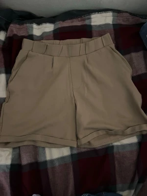 Beige midwaist shorts med fickor från lager 157 - Snygga beige shorts med midwaist passform och bred linning. Shortsen har två sidofickor fram och två dekorativa fickor bak. Tillverkade i ett mjukt och bekvämt material som passar perfekt till sommaren.