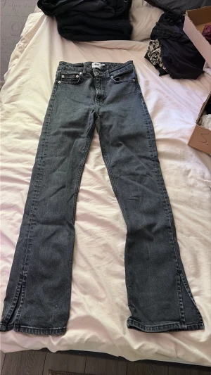 Mörkgrå bootcut jeans med slits - Snygga grå bootcut jeans med slits nertill på benen och klassiska fem fickor. Jeansen har hög midja och dragkedja med knapp framtill. Perfekta för en trendig och avslappnad stil.
