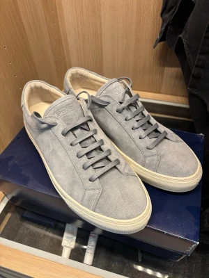 Grå mockasneakers från Polo Ralph Lauren - Stilrena sneakers i grå mocka från Polo Ralph Lauren. Klassisk låg modell med matchande grå skosnören och vit sula. Perfekta för dig som gillar en clean och tidlös look. Normal pris ca. 3000 SEK