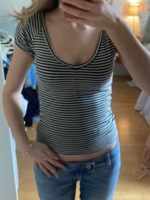 Randig topp - Säljer en svartvit, randig topp från H&M i storlek M. Toppen har en djup v-ringning, korta ärmar och är figurnära i modellen. Tillverkad i mjuk bomull som känns skön mot huden. Perfekt till jeans eller kjol för en enkel och snygg look.