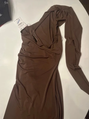 Brun långärmad omlottklänning - Säljer en snygg brun långärmad klänning från Zara med omlottdesign och v-ringning. Klänningen har en figurnära passform och är tillverkad i ett mjukt, stretchigt material som känns skönt mot huden. Perfekt för dig som gillar stilrena och trendiga plagg. Storlek M och med prislapp❤️