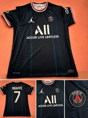 PSG fotbollströja Mbappé #7 - Mörkblå PSG matchtröja med röda och vita detaljer, tryckta loggor och sponsortryck. Mbappé #7 på ryggen. Paris Saint-Germain-emblem på bröstet och Jordan-logga. Tillverkad i lätt och ventilerande material, perfekt för fotbollsträning.