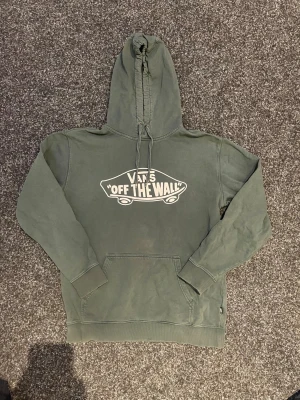Grön hoodie från Vans med tryck - Snygg grön hoodie från Vans med det klassiska 'Off The Wall'-trycket på bröstet. Hoodien har huva med dragsko och en stor magficka framtill. Perfekt för en avslappnad streetstyle-look. Kolla gärna in mina andra annonser.
