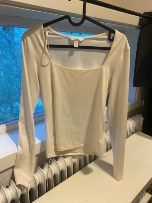Vit långärmad topp med fyrkantig ringning - Snygg vit långärmad topp med fyrkantig ringning och figurnära passform. Perfekt att styla med jeans eller kjol för en clean look. Tillverkad i mjukt material som känns skönt mot huden.
