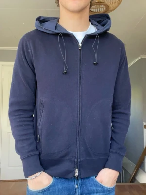 Boggi Milano zip hoodie – mörkblå – Strl 39/S - Säljer en riktigt snygg och sällsynt cardigan zip hoodie från Boggi Milano 👌 Minimal och clean design med premium känsla. Marinblå med detaljer i tekniskt tyg på huvan och axlarna.  • Märke: Boggi Milano • Storlek: 39 / S • Färg: Navy / mörkblå • Full zip framtill • Zip-fickor på sidorna • 100% bomull • Väldigt skön passform • Fint skick  Perfekt blandning mellan hoodie och lätt jacka – passar sjukt bra till jeans och vita tees 🔥  💰 Pris: 899 kr 📍 skickas