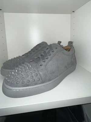 Gråa Christian Louboutin sneakers - 1:1 kopia av loubs men det står inte Christian Louboutin på boxen. Men otrolig bra kvalité. Snygga gråa sneakers i mocka från Christian Louboutin med ikoniska nitar på tån och röd sula med logga. Skorna har lågt skaft, ton-i-ton snörning och cool design som sticker ut. Perfekta för dig som vill ha något unikt och trendigt.