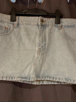 Ljusblå jeanskjol från Dr Denim - Kort ljusblå jeanskjol från Dr Denim med klassisk femficksdesign och bälteshällor. Kjolen har en rak passform och stängs med knapp och dragkedja framtill. Perfekt till sneakers eller boots för en avslappnad look.