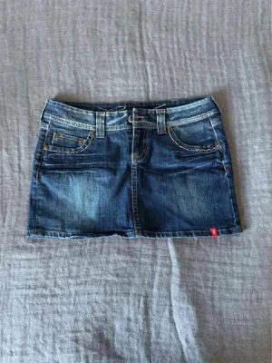 Mörkblå jeanskjol från Esprit - Super snygg mörkblå jeanskjol från Esprit med låg midja och snygga broderi detaljer. Den vintage och finns inte att köpa längre. Perfekt inför sommaren och jätte skön passform!