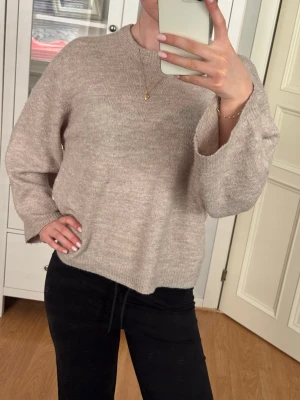Beige stickad tröja från 157 - Mysig beige stickad tröja från 157 med rund halsringning och avslappnad passform. Tröjan har långa ärmar och ribbade muddar vid halsen. 
