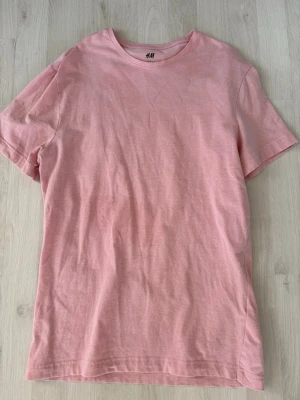 Ljusrosa t-shirt från H&M - En basic ljusrosa t-shirt från H&M med rund halsringning och korta ärmar. Tillverkad i mjuk bomull som känns skön mot huden. Perfekt för en avslappnad och stilren look. OBS fläck på tröjan!