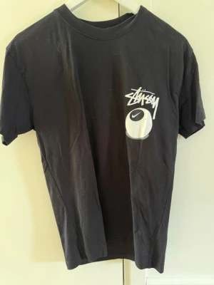 Svart Stüssy x Nike t-shirt - Svart t-shirt från Stüssy och Nike med vit logga och grafiskt tryck både fram och bak. Klassisk passform med rund hals och korta ärmar. Tillverkad i mjuk bomull, perfekt för en streetwear-look .  Ej @kta men snygg ändå 