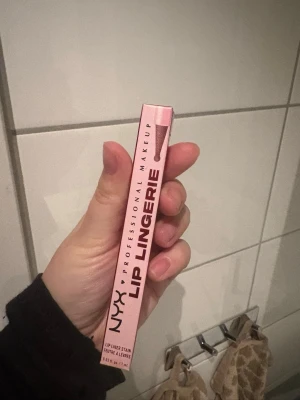NYX Lip Lingerie läppenna rosa - NYX Professional Makeup Lip Lingerie läppenna i en snygg rosa nyans. Pennan har en smal och praktisk form som gör det enkelt att definiera läpparna. Förpackningen är rosa med tydlig logga och produktnamn.