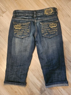 Y2K 2000's Capris Victoria Beckham Inspirerat - Äkta 2000-tals jeans som jag köpte på Vinted! Tyvärr är de för små för mig.  De har flera kronor på dem och liknar Victoria Beckhams jeans! Det finns dessutom text på fickorna. På framsidan finns det en krona.  OBS!!! De är troligen inte en S då de är 34cm tvärs över midjan. Blixtlåset har gått sönder.  