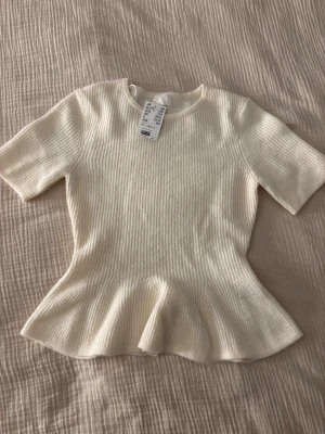 Vit ribbad topp med volangkant - Superfin vit ribbad topp från H&M med korta ärmar och volangkant nedtill. Helt oanvänd!❣️