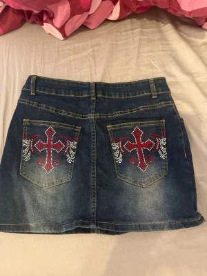 Mörkblå jeanskjol med broderade fickor - Snygg mörkblå jeanskjol med broderade bakfickor i rött och vitt. Stolek S 💕aldrig använda då jag inte tyckte de var min stil