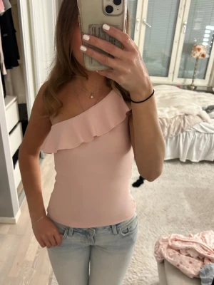 Ljusrosa one shoulder topp Stradivarius - Säljer en ljusrosa one shoulder topp från Stradivarius. Toppen har en volangdetalj längs halsringningen och sitter figurnära. 