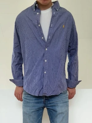 Blå Randig Ralph Lauren skjorta - Blå Randig Ralph Lauren skjorta i bra skivk utan nåra defekter. Strl L men sitter som en M och hör gärna av er vid frågor elr funderingar!!