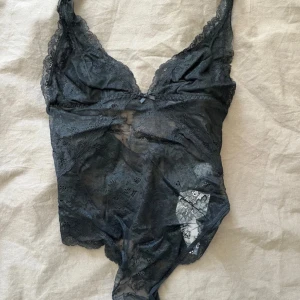 Svart spetsbody från H&M - Snygg svart body i spets från H&M med djup v-ringning och tunna axelband. Bodyn har transparent spetsmaterial och dekorativa detaljer både fram och bak. Perfekt för dig som gillar en trendig och feminin look. Aldrig använd med prislapp kvar 
