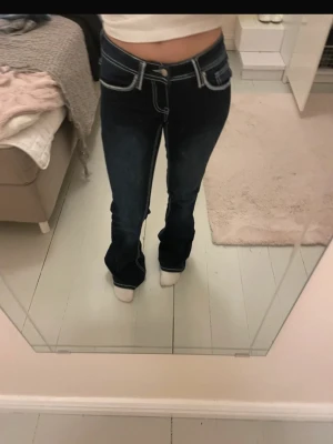 Mörkblå bootcut jeans med kontrastsömmar - Säljer ett par mörkblå bootcut jeans med vita kontrastsömmar och låg midja. Jeansen har dekorativ brodyr på bakfickan och klassisk femficksdesign. Perfekta för dig som gillar en retro vibe och vill sticka ut lite extra. Ifrån ryvls i storlek 158.☺️