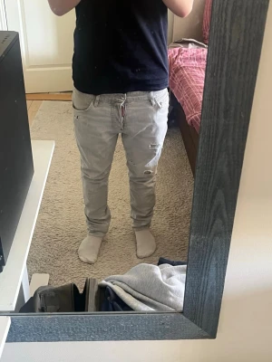 Gråa slitna jeans från Dsquared2 - Säljer ett par gråa jeans från Dsquared2 med slitna detaljer och klassisk femficksmodell. Jeansen har en rak passform och är tillverkade i mjuk bomull. Perfekta för dig som gillar en avslappnad och trendig stil.