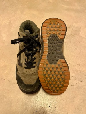 Gröna fodrade Vans med svarta detaljer - Säljer ett par gröna fodrade Vans med svarta detaljer och snörning. Skorna har en robust gummisula, samt en mjuk, fodrad insida. 