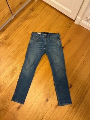 Blå slim fit jeans från Replay - Snygga blå slim fit jeans från Replay med klassisk femficksdesign och dragkedjegylf. Jeansen har en något tvättad look och är perfekta för en avslappnad stil. Materialet är en denim som ger bra komfort.