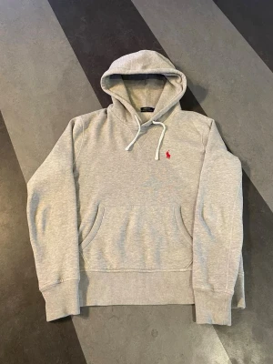Grå hoodie från Polo Ralph Lauren - Tjenare! Säljer denhära feta gråa ralph lauren hoodien med ett snyggt rött märke. Det är en storlek S men passar mer som en XS. Bara att höra av sig vid frågor.