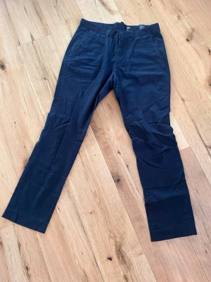 Mörkblå kostymbyxor från H&M - Snygga mörkblå kostymbyxor från H&M med klassisk rak passform och diskreta sidofickor. Tillverkade i ett mjukt tyg som ger en clean look. Perfekta för dig som vill ha en stilren och enkel byxa till garderoben.
