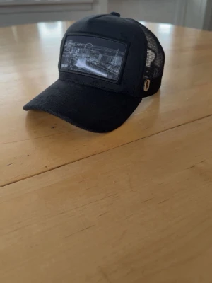 Keps från one cap  - Snygg svart keps med böjd skärm och mesh på sidorna och bak. Framtill finns ett svartvitt tryck med stadsmotiv. Justerbar snapback baktill för perfekt passform. Perfekt accessoar för en cool och avslappnad stil. Trycket är en bild på LAS vegas 