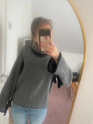 Grå stickad polotröja med svarta detaljer - Mysig grå stickad polotröja med svarta kanter vid ärmslut och krage. Tröjan har vida ärmar och en avslappnad passform. 