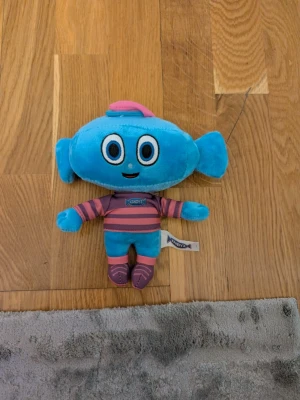 Blå Kandyz-mjukisdjur - Säljer ett gulligt blått mjukisdjur från Kandyz med stora öron och randig tröja i rosa och lila. Dockan har stora broderade ögon, ett leende och små skor i matchande färger. Perfekt som present eller dekoration!