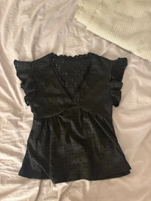 Svart topp med volangärmar och spets - Snygg svart topp med v-ringning, volangärmar och spetsdetaljer vid halsen. 