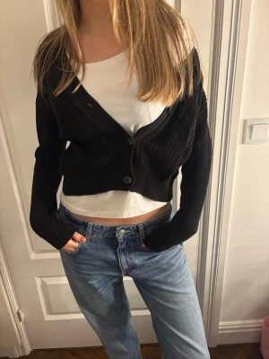 Svart cropped kofta med knappar - Säljer en svart, ribbstickad cropped kofta med två knappar framtill. Koftan har lång ärm och en avslappnad passform som passar perfekt till jeans. Från lager 157💕