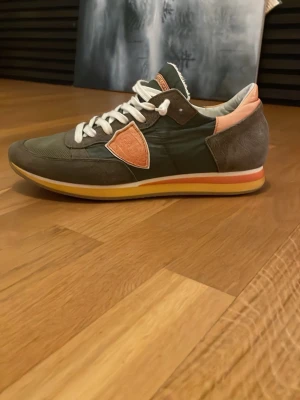 Philippe Model sneakers grön/orange - Snygga sneakers från Philippe Model i grönt tyg och mocka med orange detaljer och vit sula med orange rand. Skorna har vita skosnören och en låg profil. 