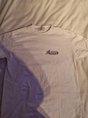 Vit Casablanca t-shirt med tryck - Säljer en vit t-shirt från Casablanca med trycket 'Aiiiiiir' på bröstet och en stor färgglad grafik med flygplan och texten Casablanca på ryggen. Klassisk passform och rund hals. Perfekt för dig som gillar streetwear och snygga prints.