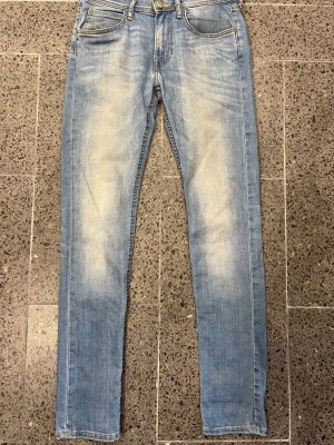 Lee Luke W28/L32 - Väldigt fint skick - Säljer ett par ljusblå skinny jeans från Lee med klassisk femficksmodell och slitna detaljer framtill. Jeansen har gul kontrastsöm och knapp med Lee-logga. Perfekta för en avslappnad och trendig look.