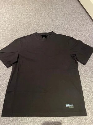 Svart t-shirt från H&M  - Svart t-shirt från H&M med relaxed fit. Klassisk rund halsringning och korta ärmar. Perfekt basic-plagg med tryck på ryggen och diskret Coolmax-logga nere vid fållen. Skön och enkel stil för alla tillfällen. Lite slitet på trycket.