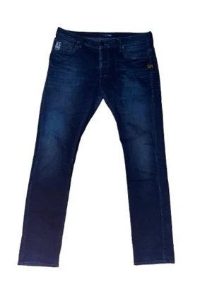 Mörkblå jeans från G-Star - Snygga mörkblå jeans från G-Star med raka ben och klassisk femficksmodell. Jeansen har diskreta slitningar och G-Star-logga på bakfickan. Tillverkade i stretchigt denim för extra komfort och en schysst passform.