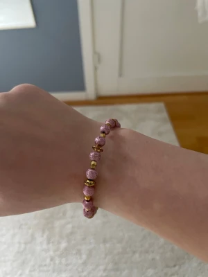 Två fina rosa lilla guld armband - Snyggt armband med lila glittriga pärlor och små guldfärgade detaljer. Pärlorna är runda och sitter på en elastisk tråd som gör det enkelt att ta på och av. Perfekt accessoar för att addera lite färg och bling till din outfit.