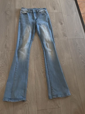 Ljusblå bootcut jeans med fickdetalj - Säljer ett par ljusblå bootcut jeans med snygg slitning framtill och dekorativ ficka bak med knapp. Jeansen har klassisk femficksmodell och är tillverkade i mjukt denimtyg. Perfekta för en avslappnad och trendig look. Använda 2-3 gånger . Sitter jätte fint på och känns som mjukis och är super sköna på känns inte alls som jeans när man har de på . 