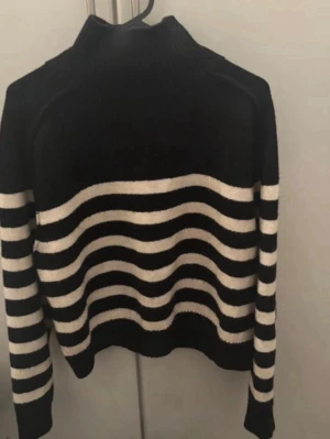 Svartvit randig stickad tröja - Säljer en svart stickad tröja med vita vågiga ränder. Tröjan har hög krage och långa ärmar, perfekt för att hålla värmen. Den har en avslappnad passform och är riktigt mjuk och skön.   För mer bilder/justering av pris skriv gärna❤️🤗