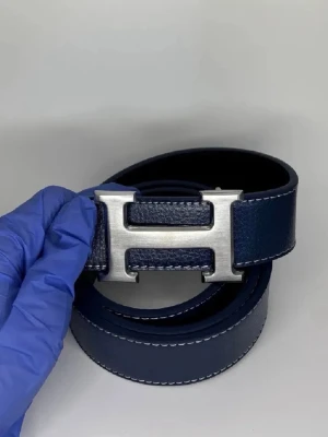 Mörkblått H skärp i skinn - Snyggt mörkblått skärp från H med klassiskt H-spänne i silverfärgad metall. Bältet är gjort i äkta skinn och har vita kontrastsömmar längs kanterna. Perfekt accessoar för att lyfta din outfit.