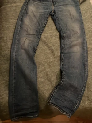 Blå raka jeans med slitningar - Ett par blå jeans med rak passform och snygga slitningar på benen. Jeansen har klassisk femficksdesign och tydliga tvättade detaljer för en avslappnad look. Perfekta för dig som gillar en tidlös och cool stil. 30W 34L