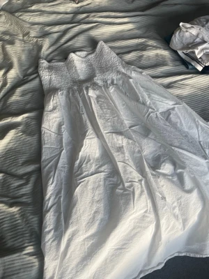 Vit smockad kjol från Gina Tricot - Supersöt vit kjol från Gina Tricot med smockad midja och lätt utställd passform. Kjolen är gjord i mjuk bomull och har en luftig känsla som passar perfekt till varma dagar. Enkel att styla med crop tops eller oversized tröjor.