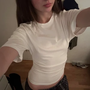 Vit tight t-shirt med rynkade sidor - Säljer en vit, figurnära t-shirt med rynkade detaljer på sidorna. T-shirten har korta ärmar och rund halsringning. Perfekt för dig som gillar en enkel men ändå trendig look. Osäker på om plagget är nytvättat eller ej så ifall tvätt önskas är det bara att skriva😊