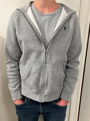 Grå Polo Ralph Lauren hoodie - Snygg grå hoodie med dragkedja från Polo Ralph lauren med blått märke på bröstet.