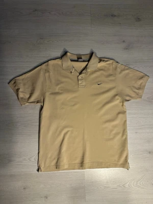 Nike Piké - Klassisk beige pikétröja från Nike med liten svart logga på bröstet. Perfekt för en avslappnad och sportig stil. Skriv vid frågor och kolla gärna in min profil för fler feta plagg! 