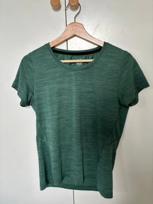 Grön träningströja från SOC - s - Sportig grön träningströja från SOC med rund halsringning och korta ärmar. Tillverkad i ett lätt och snabbtorkande funktionsmaterial med diskret mönster och meshpanel på ryggen för extra ventilation. Perfekt för löpning eller gym.